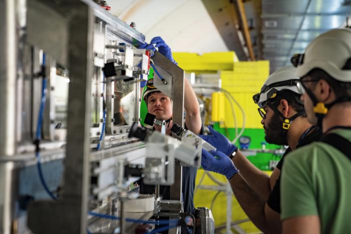 three men working on equipment wearing helmets